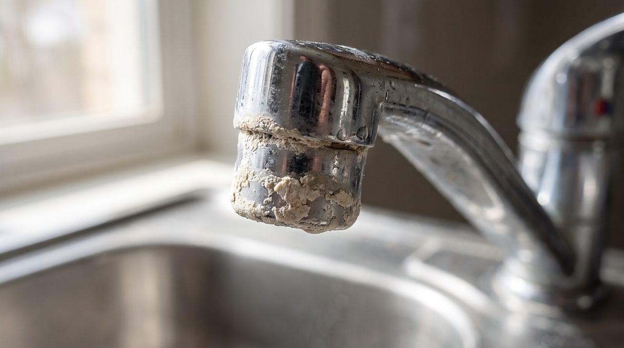 crusty white mineral scale ring built up around a kitchen faucet spout opening