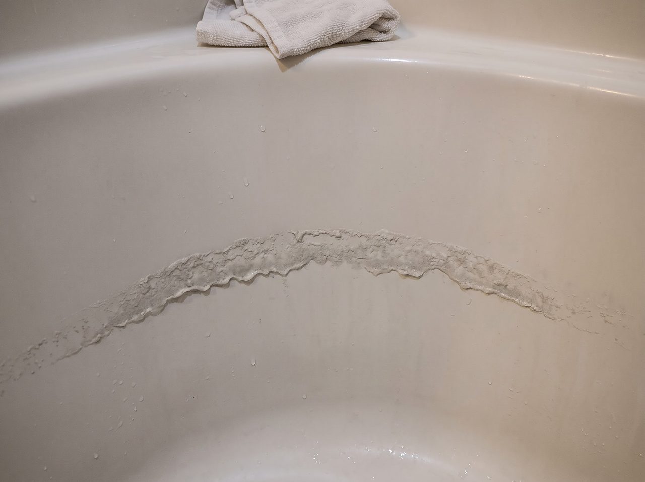 grayish soap scum ring built up along a bathtub wall from hard water