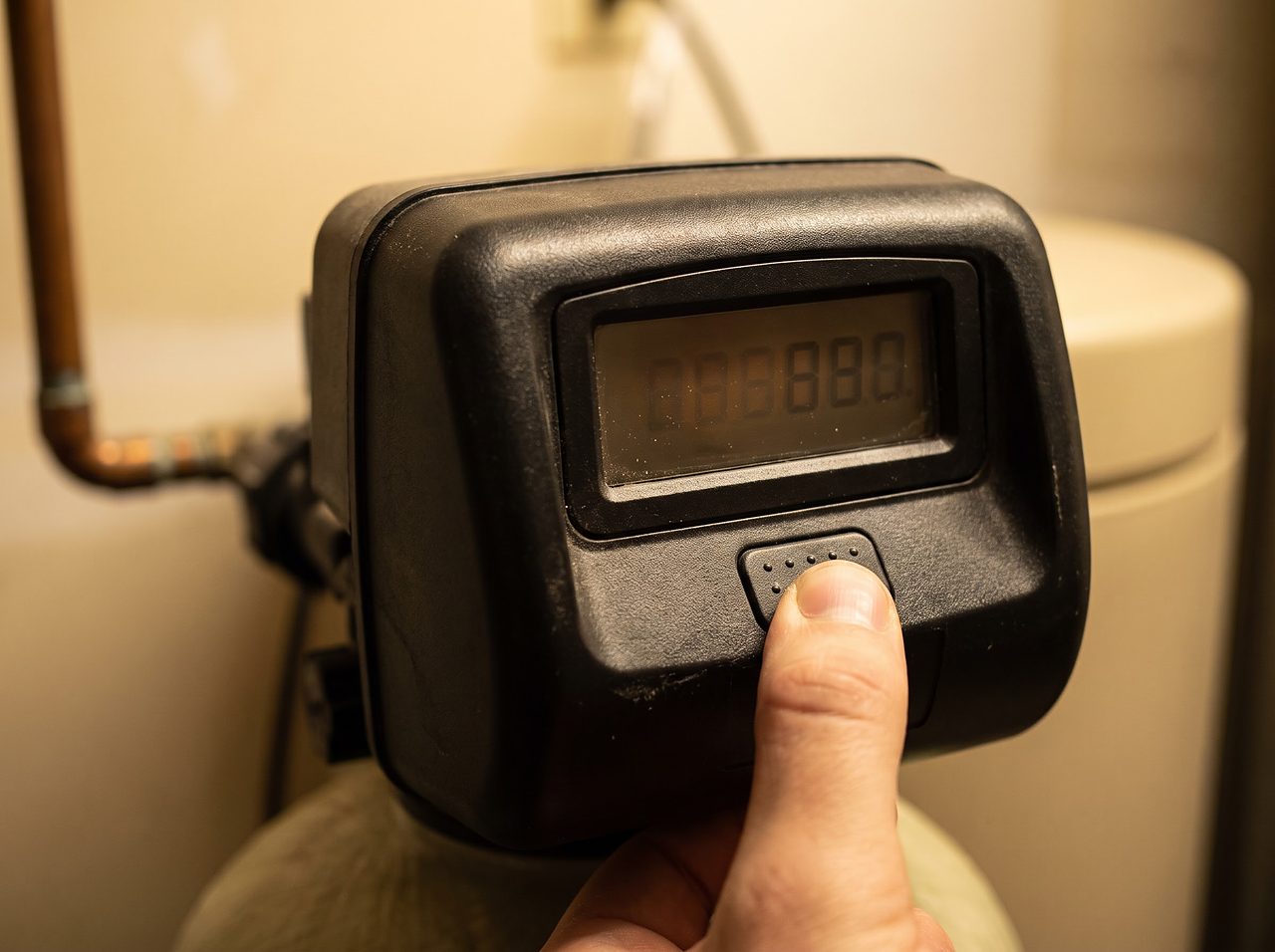 hand adjusting a water softener control panel while checking the hardness setting
