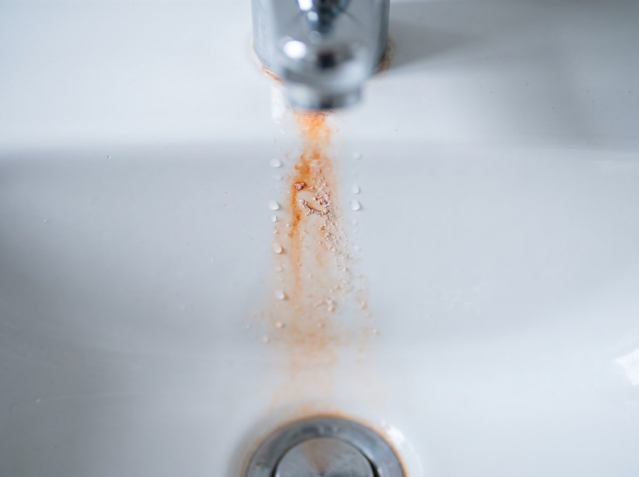 reddish iron staining trailing down a porcelain sink basin near the drain